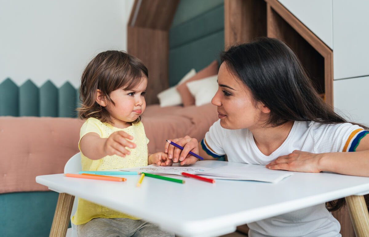 Nounou expérimentée et petite fille de 3 ans concentrées sur un dessin coloré lors d'une séance de babysitting à domicile à Paris