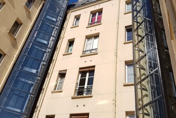 Ascenseur modernisé monte-charge immeuble ancien Paris beffroi verre façade crème fenêtres mansardées conciergerie travaux