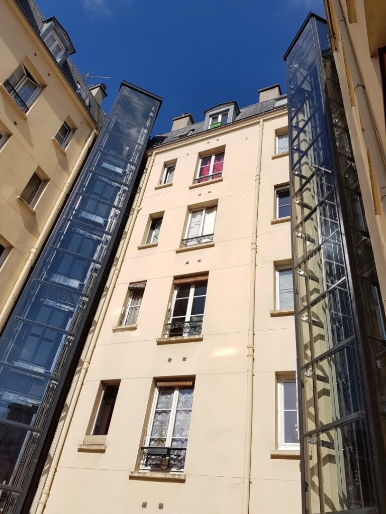 Ascenseur modernisé monte-charge immeuble ancien Paris beffroi verre façade crème fenêtres mansardées conciergerie travaux