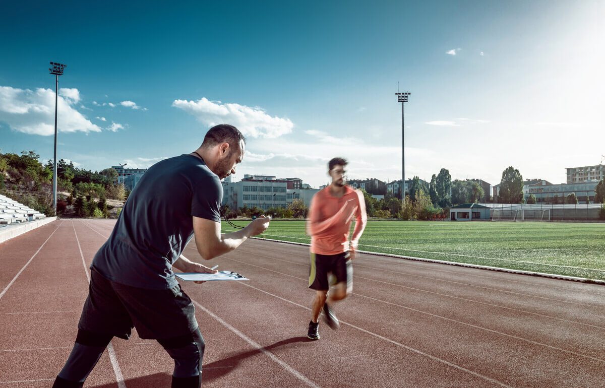 Coach sportif clipboard guide coureur tenue orange stade piste rouge préparation marathon Paris.
